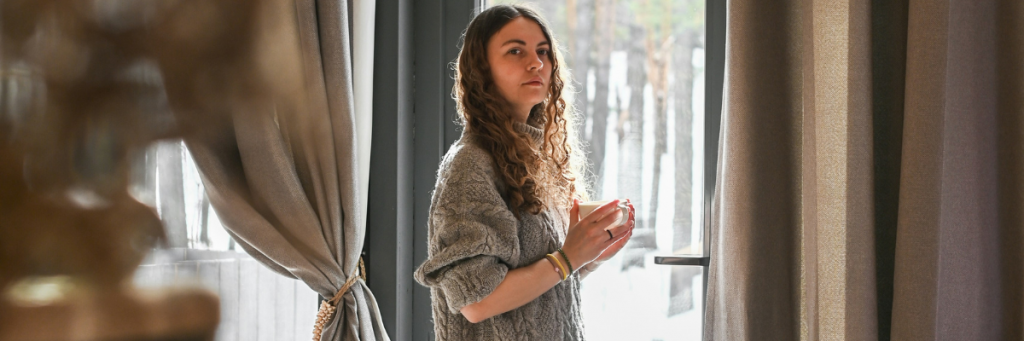 Lady holding cup looking into distance in front of window