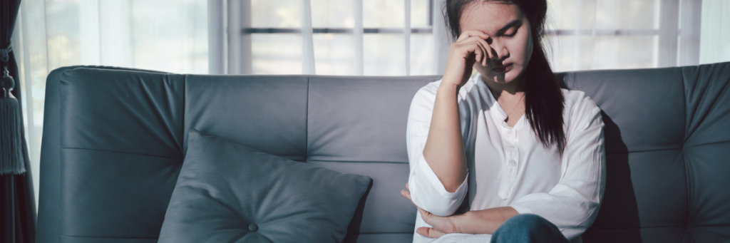 Woman looking tired and overwhelmed head in hand sitting on sofa